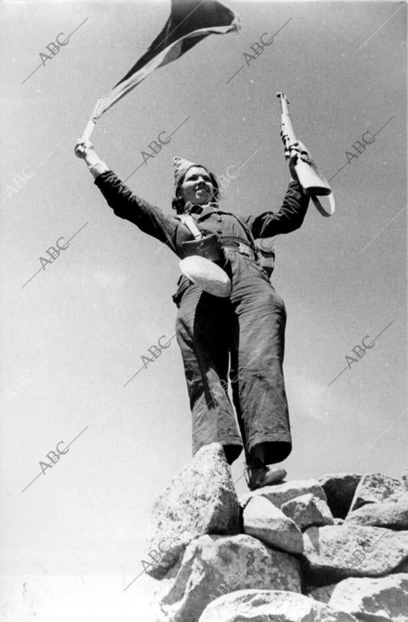 Miliciana saludando a sus camaradas de la columna Mangada, con la bandera Republicana, cogida a las tropas nacionales que se hicieron pasar por republicanos, con saludos y Emblemas del Frente Popular, para engañarles.