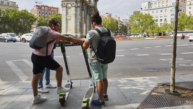 Dos jóvenes cogen dos patinetes de la compañía Lime, frente a la Puerta de Alcalá