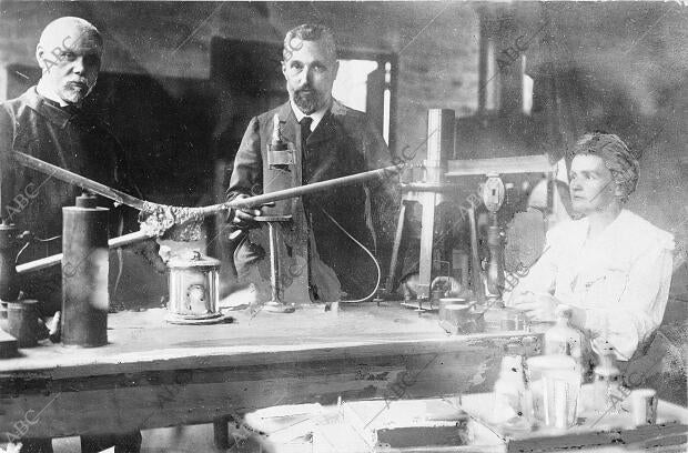 Marie Curie junto a su esposo, en el centro, en su laboratorio, acompañados del...