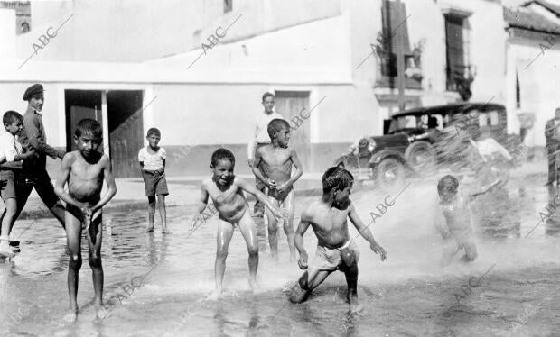 Grupo de muchachos tomando duchas de una manga de riego en plena calle