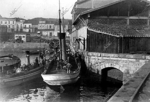 1931 Parejas de barcos descargando en la lonja de pescado del puerto de la...