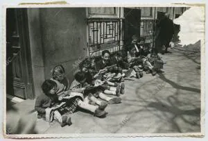 Unos niños en la calle, sentados en el suelo, leyendo tebeos