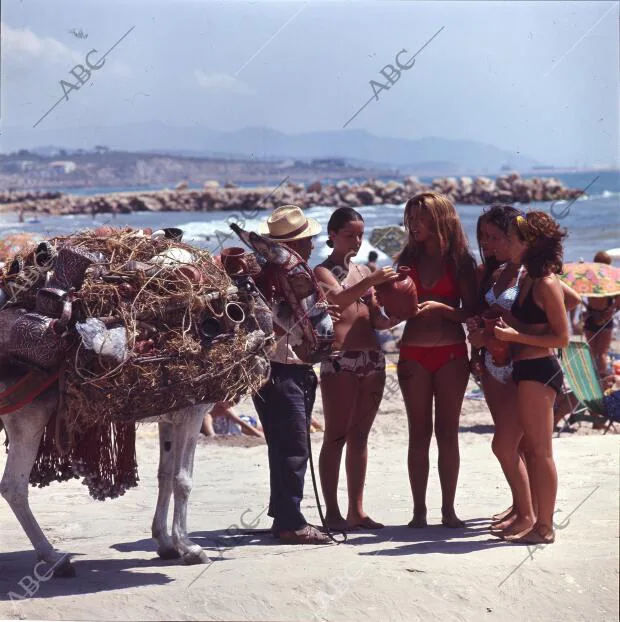 Un vendedor de cerámica con unas jóvenes turistas en bikini, mirando un botijo