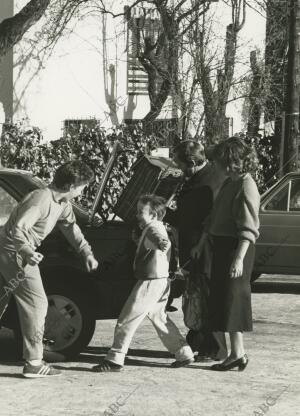 Dos niños juegan al lado del coche de sus padres, mientras estos meten el carro...