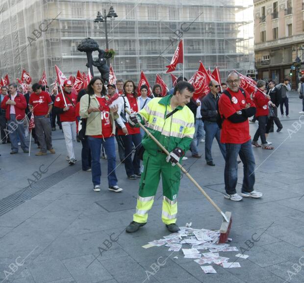 Un barrendero trabaja ante las miradas de unos manifestantes, en la puerta del...