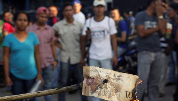 Unos venezolanos queman un billete de cien bolívares, durante una protesta en El Pinal